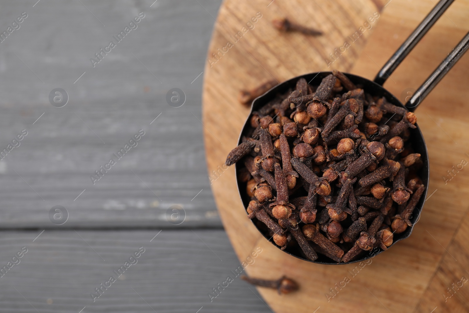 Photo of Aromatic cloves in scoop on grey wooden table, top view. Space for text
