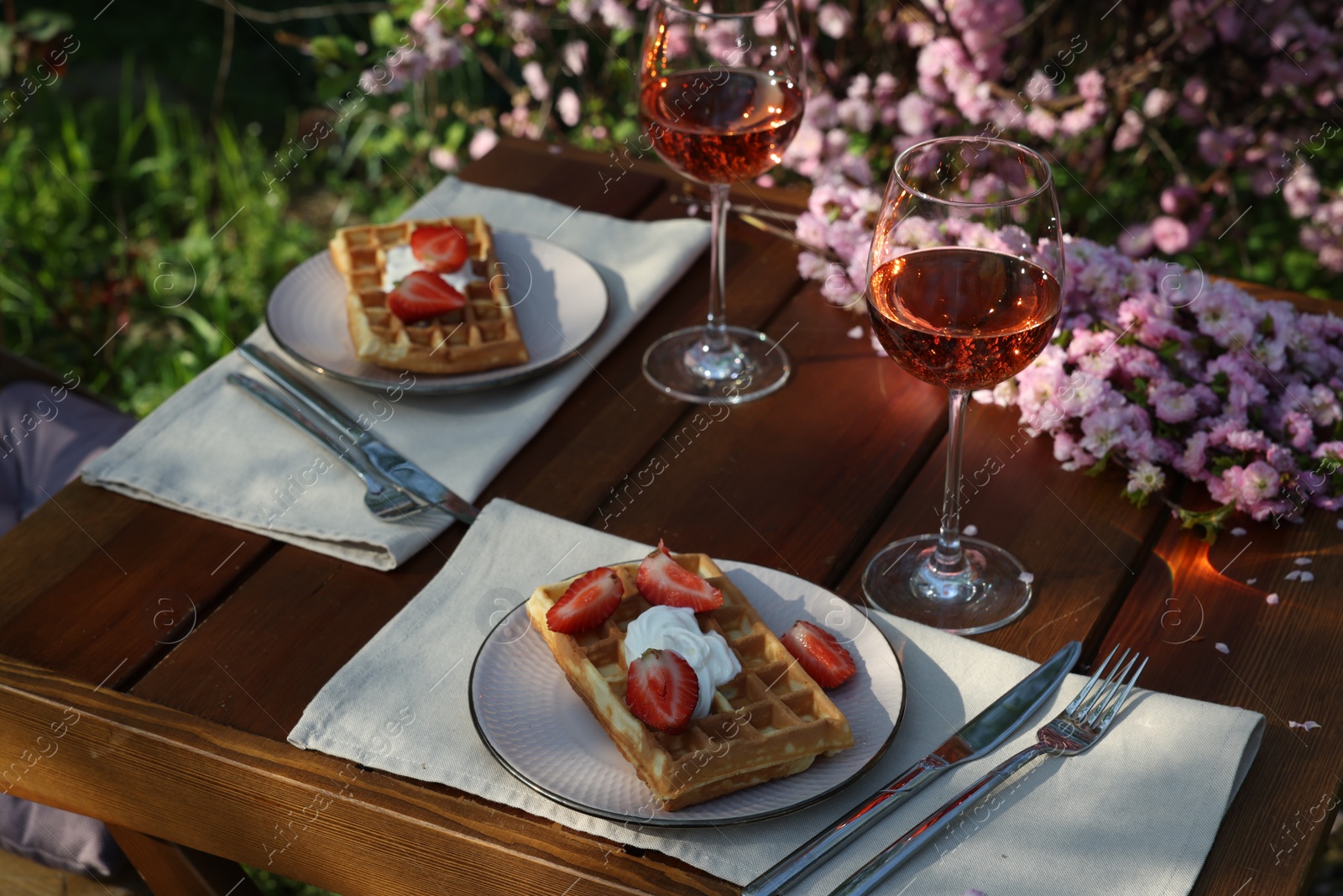 Photo of Delicious Belgian waffles with fresh strawberries and wine served on table in garden