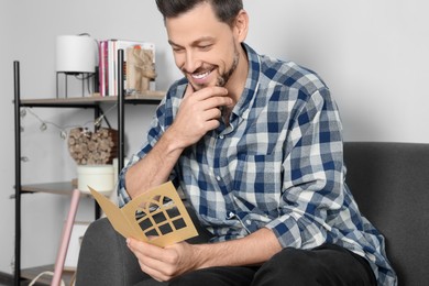 Happy man reading greeting card on sofa in living room