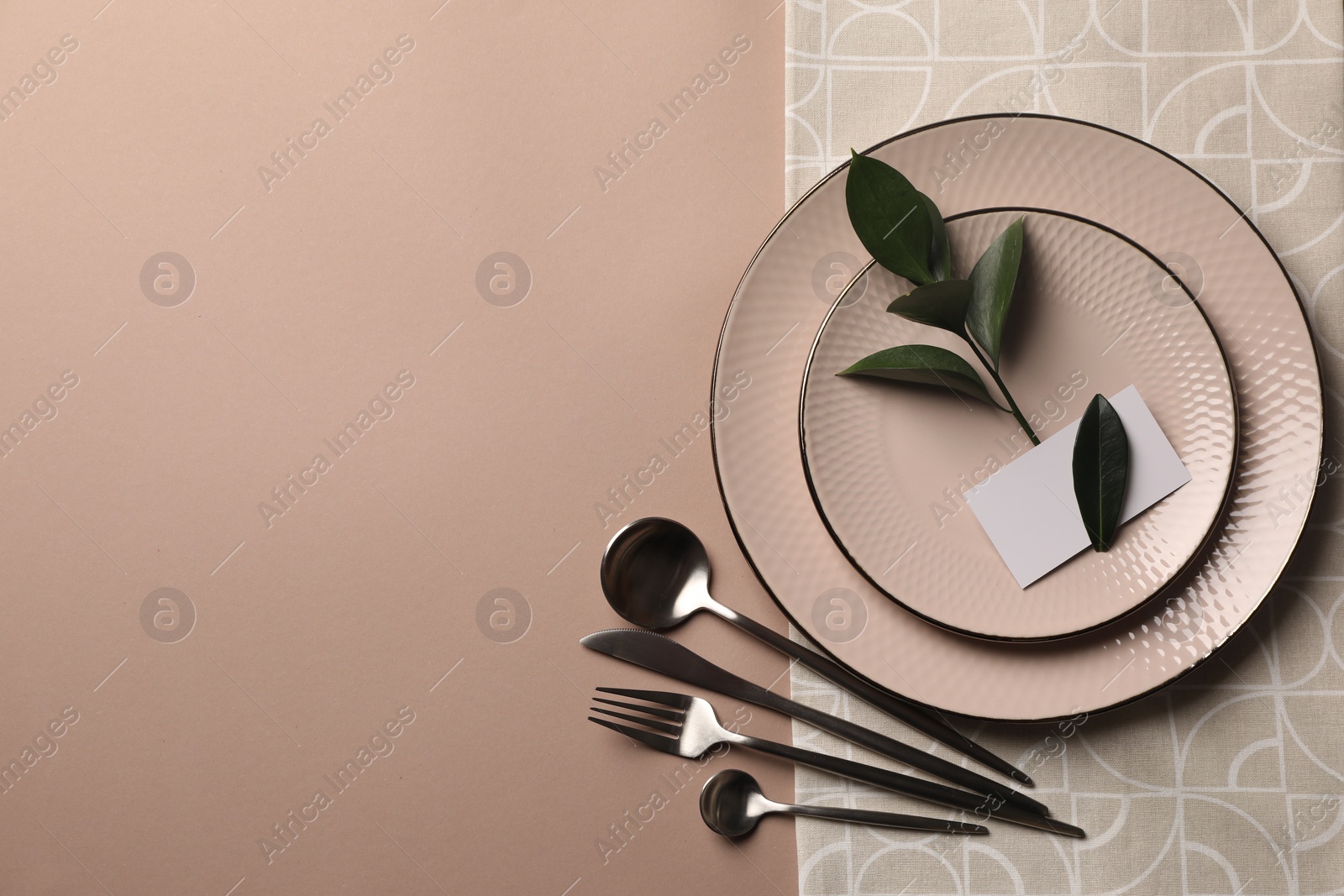 Photo of Stylish table setting. Plates, cutlery, blank card and green twig on beige background, top view with space for text