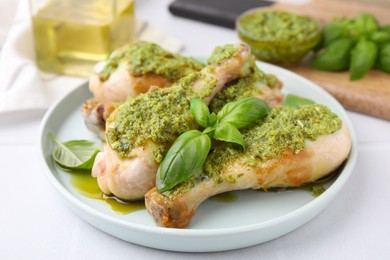 Photo of Delicious fried chicken drumsticks with pesto sauce and basil on white table, closeup