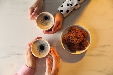 Photo of Women with cups of hot coffee and cookies at white marble table, top view