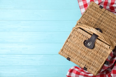 Photo of Closed wicker picnic basket and checkered blanket on wooden table, top view. Space for text