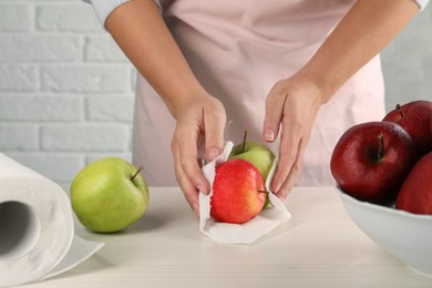 Photo of Woman wiping apples with paper towel at light wooden table, closeup