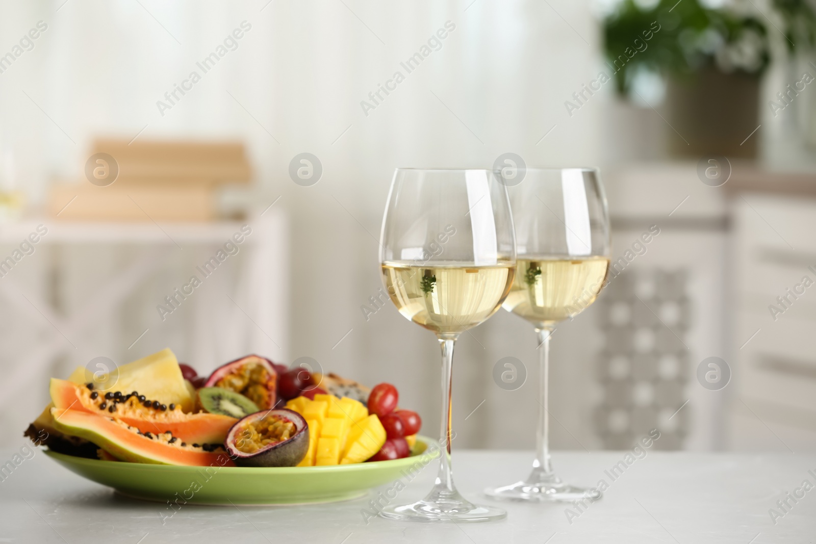 Photo of Delicious exotic fruits and glasses of wine on white table indoors