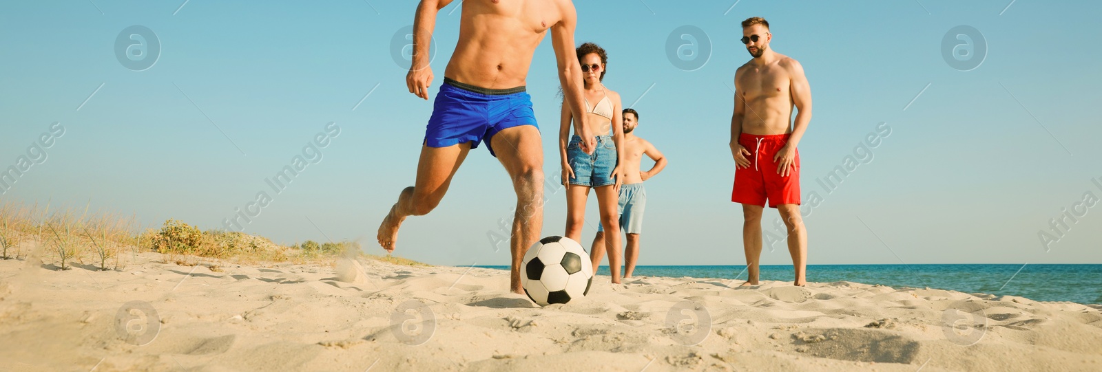 Image of Group of friends playing football on sandy beach, low angle view. Banner design