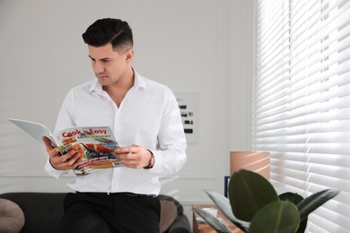 Photo of Man reading culinary magazine near window indoors