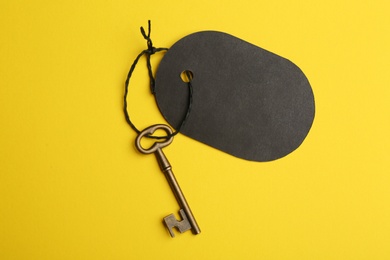 Photo of Vintage key with blank tag on yellow background, top view. Keyword concept