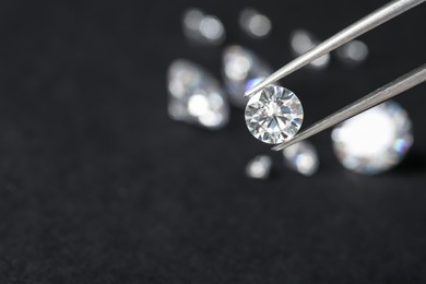 Photo of Tweezers with beautiful shiny diamond against dark blurred background, closeup. Space for text