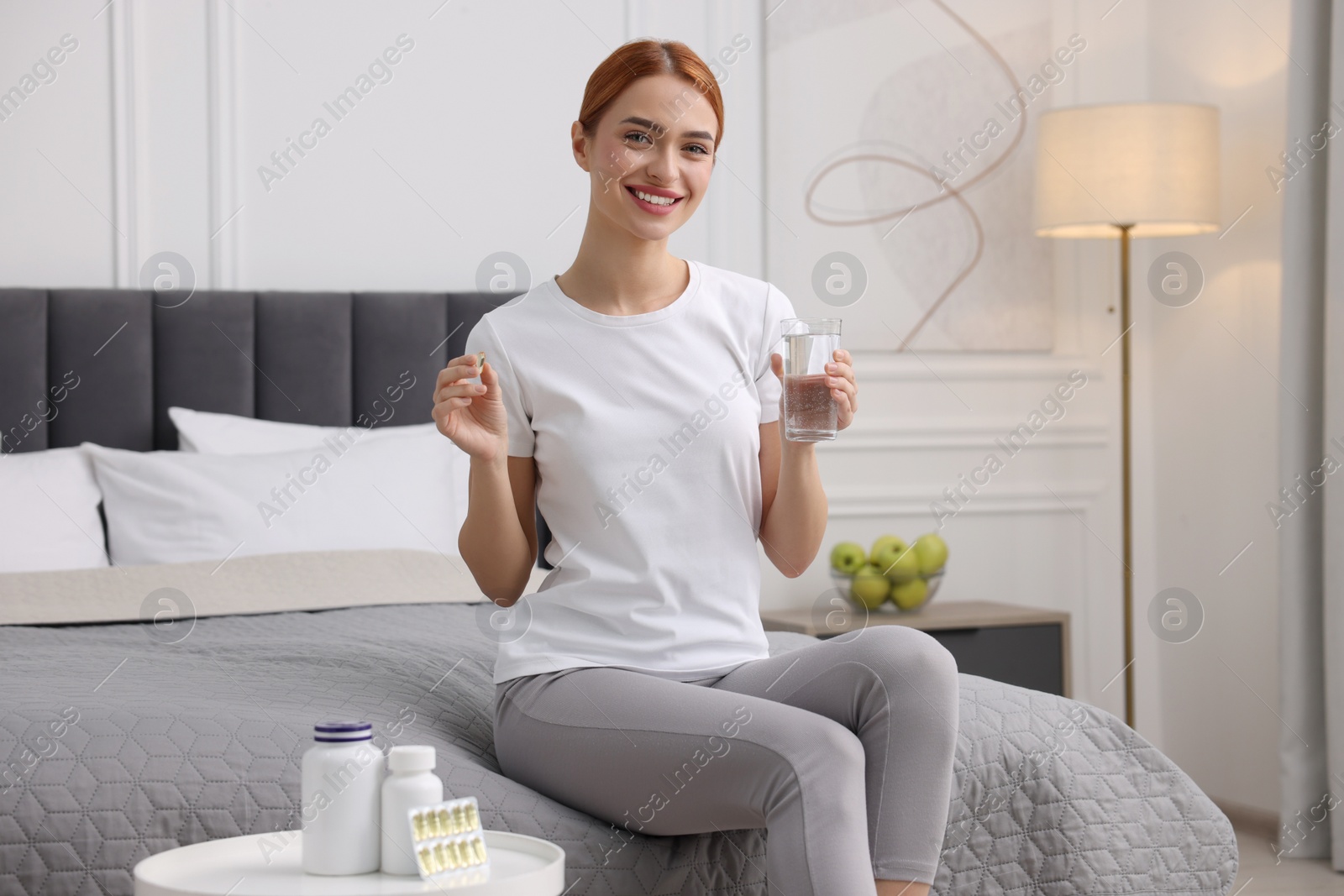 Photo of Happy young woman with pill and glasswater in room. Weight loss