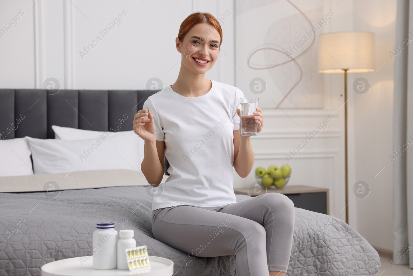 Photo of Happy young woman with pill and glass of water in room. Weight loss