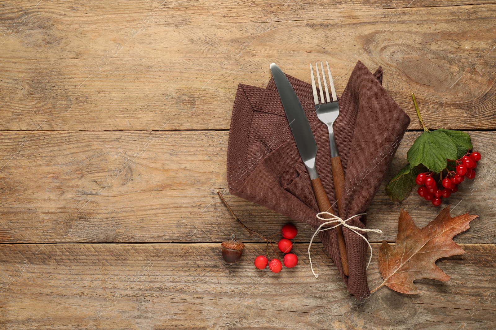 Photo of Autumn table setting. Cutlery, napkin and berries on wooden background, flat lay with space for text