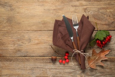 Photo of Autumn table setting. Cutlery, napkin and berries on wooden background, flat lay with space for text