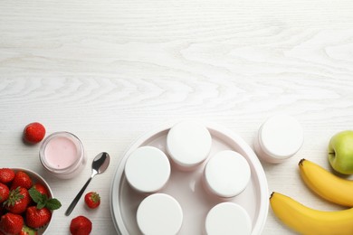 Yogurt maker with jars and different fruits on white wooden table, flat lay. Space for text