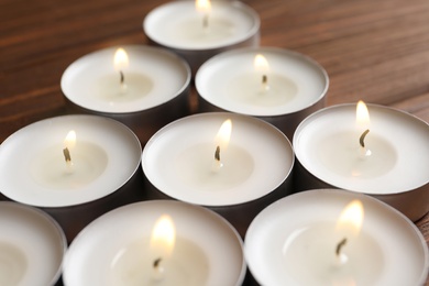 Photo of Small wax candles burning on wooden table, closeup