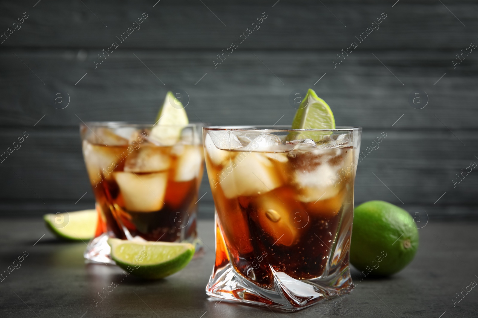 Photo of Glasses of cocktail with cola, ice and cut lime on table