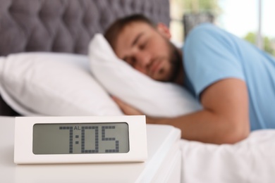 Alarm clock on table and young man sleeping in bed at home