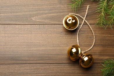 Golden sleigh bells with rope and fir branches on wooden background, flat lay. Space for text