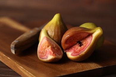 Photo of Tasty raw figs and knife on wooden board, closeup