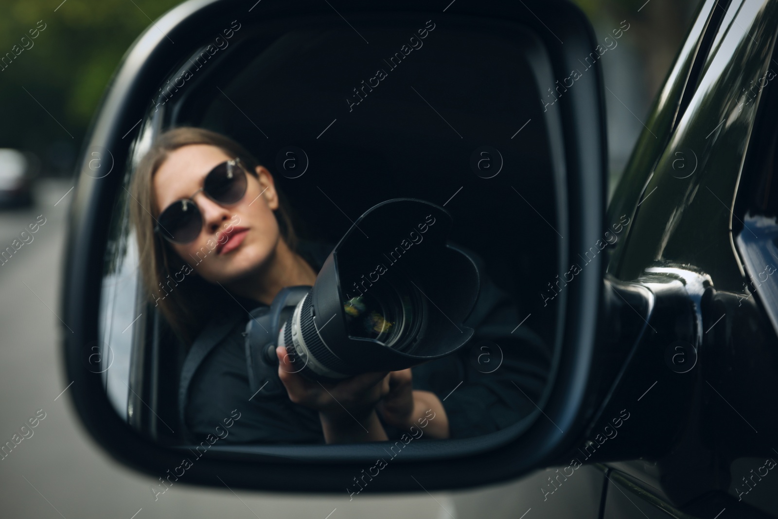 Photo of Private detective with camera spying from auto, view through car side mirror