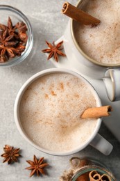 Photo of Cups of delicious eggnog with anise and cinnamon on light grey table, flat lay
