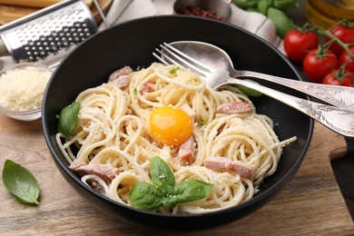 Bowl of delicious pasta Carbonara with egg yolk and cutlery on wooden table, closeup