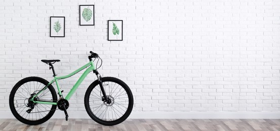 Image of Modern green bicycle near white brick wall indoors, space for text. Banner design
