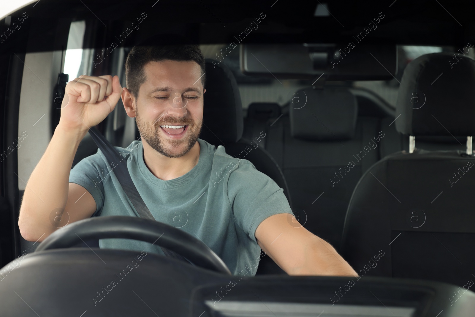 Photo of Listening to radio. Handsome man enjoying music in car, view through windshield