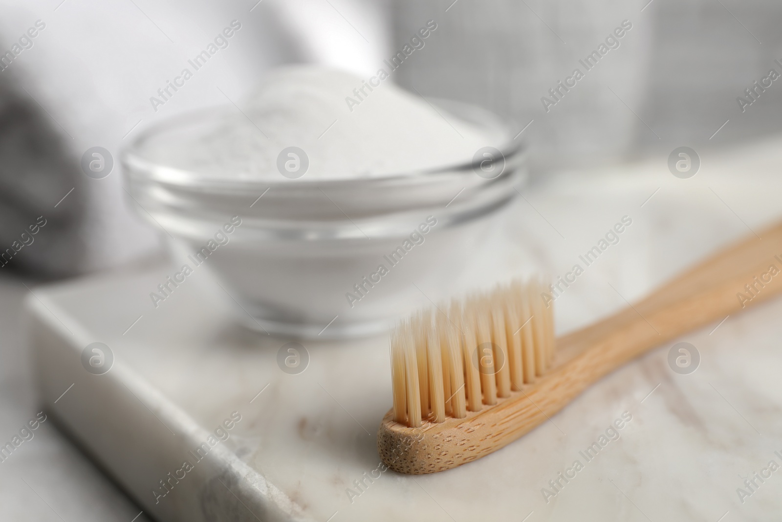 Photo of Bamboo toothbrush and glass bowl of baking soda on marble board, closeup. Space for text