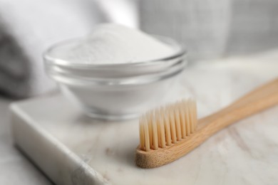 Photo of Bamboo toothbrush and glass bowl of baking soda on marble board, closeup. Space for text