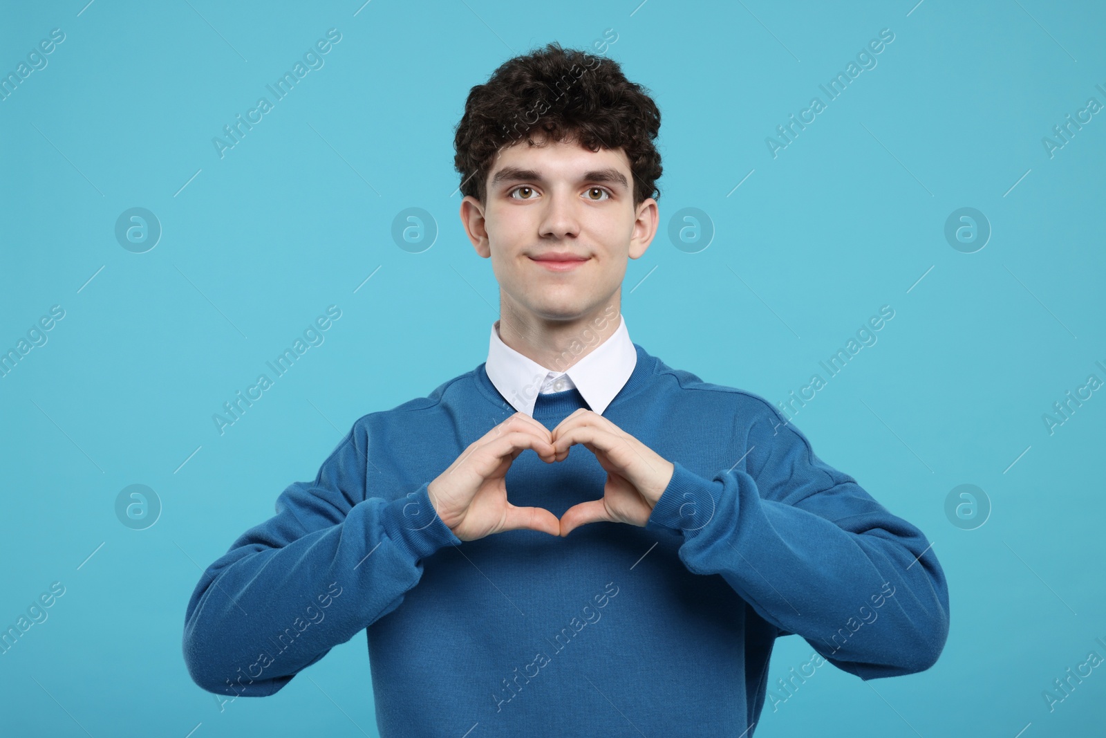 Photo of Happy young man showing heart gesture with hands on light blue background