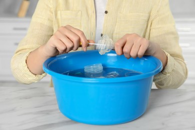 Woman washing baby bottle nipple above basin at white marble table, closeup