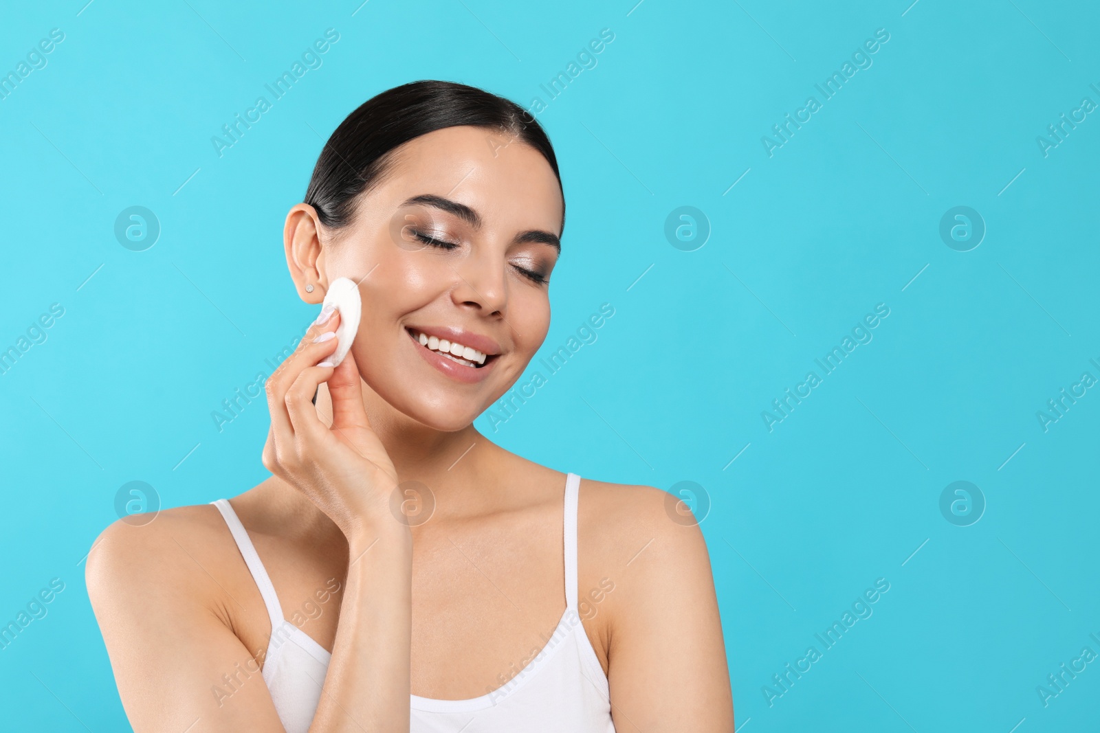 Photo of Young woman using cotton pad with micellar water on light blue background, space for text