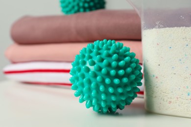 Photo of Turquoise dryer ball and detergent on white table, closeup