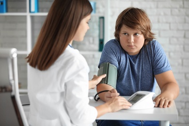 Female doctor checking overweight boy's blood pressure in clinic