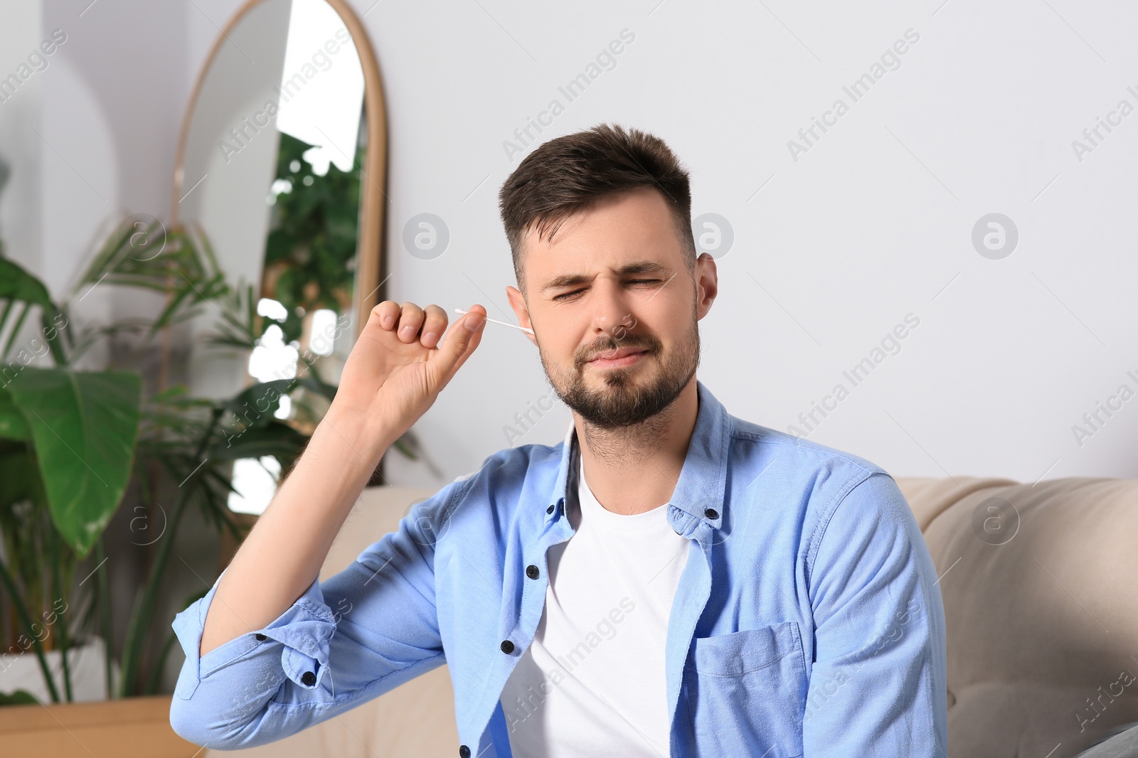 Photo of Young man cleaning ear with cotton swab at home