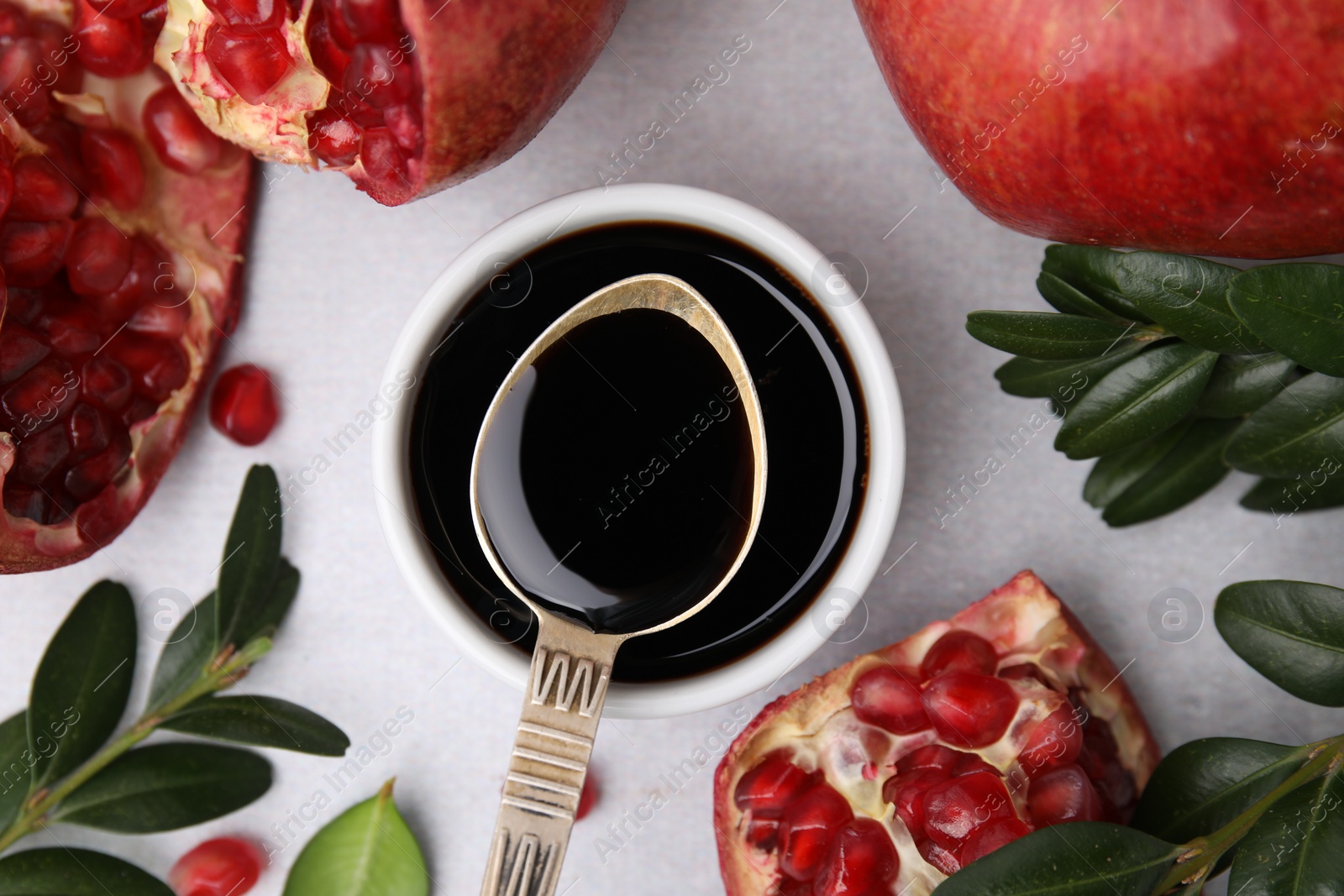 Photo of Tasty pomegranate sauce, branches and fruits on light table, flat lay