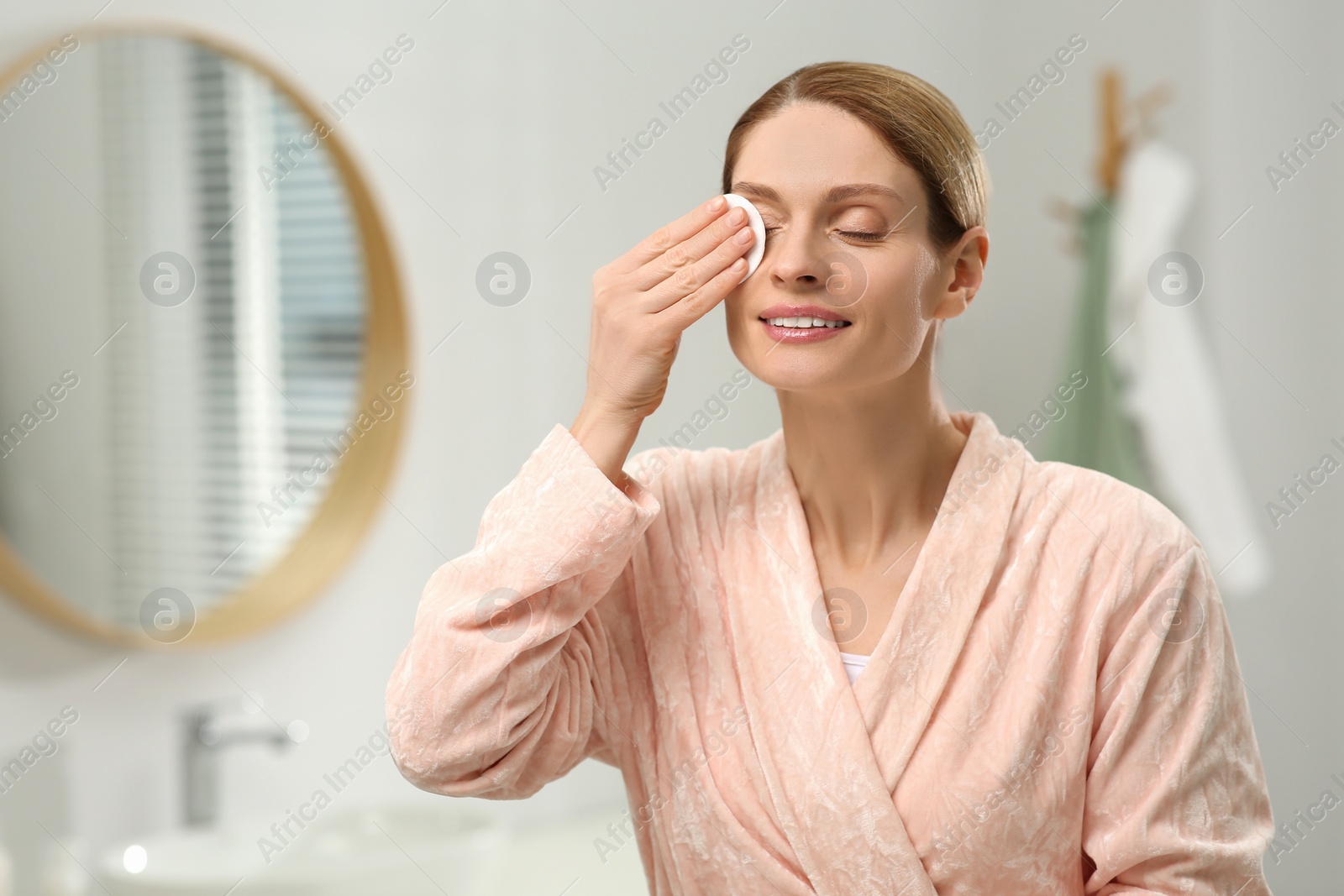 Photo of Beautiful woman removing makeup with cotton pad indoors, space for text