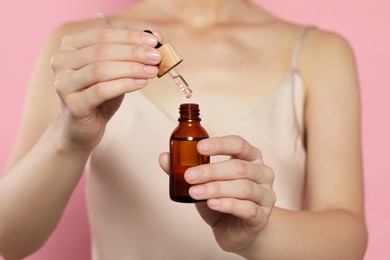 Young woman with bottle of essential oil on pink background, closeup