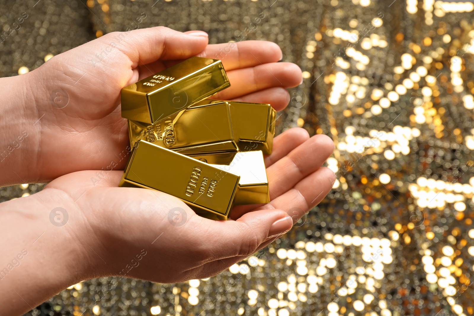 Photo of Woman holding shiny gold bars against sequin fabric, closeup