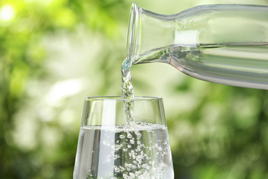 Photo of Pouring water from bottle into glass on blurred background