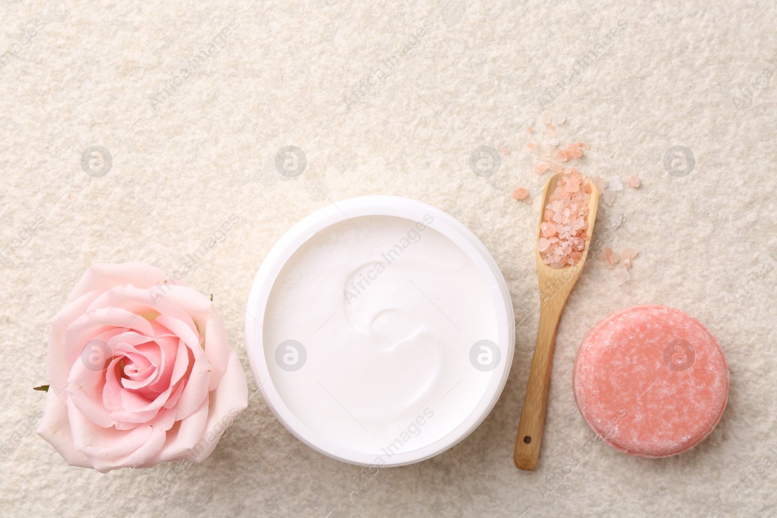 Photo of Flat lay composition with moisturizing cream in open jar and other body care products on light textured table