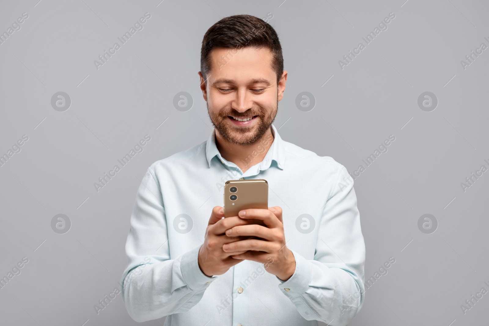 Photo of Happy man sending message via smartphone on grey background