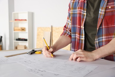 Handyman working with blueprints at table in room, closeup