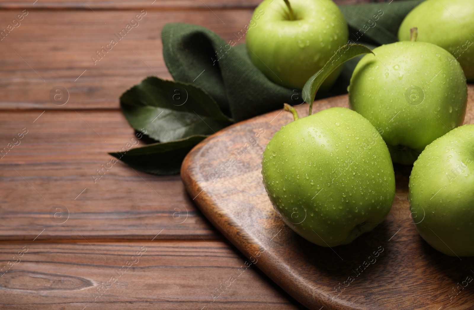 Photo of Ripe green apples with leaves and water drops on wooden table, closeup. Space for text