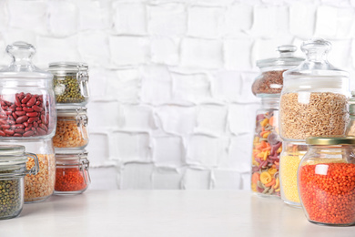 Photo of Jars with different cereals on white table against brick wall. Space for text