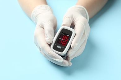 Photo of Doctor in gloves holding fingertip pulse oximeter at light blue background, closeup