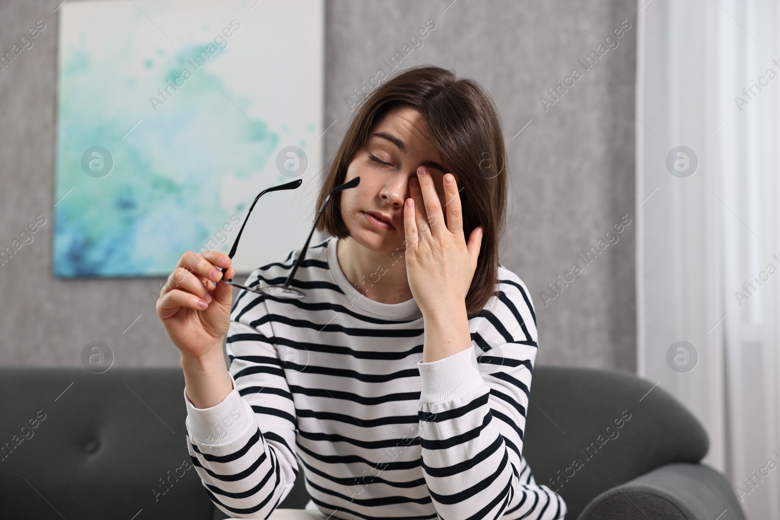 Photo of Overwhelmed woman with glasses sitting on sofa indoors