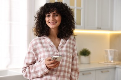 Photo of Beautiful young woman in stylish pyjama with smartphone in kitchen