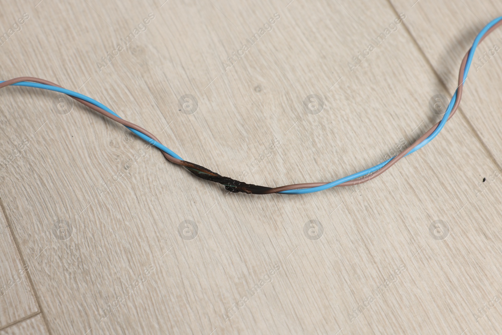 Photo of Burnt wires on wooden floor, above view. Electrical short circuit